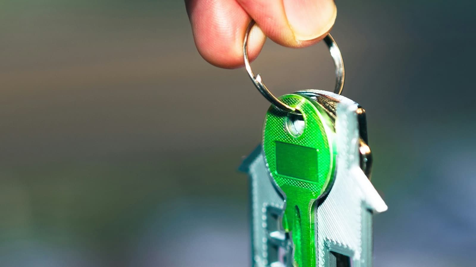 Mano che solleva un portachiavi a forma di casetta con una chiave verde