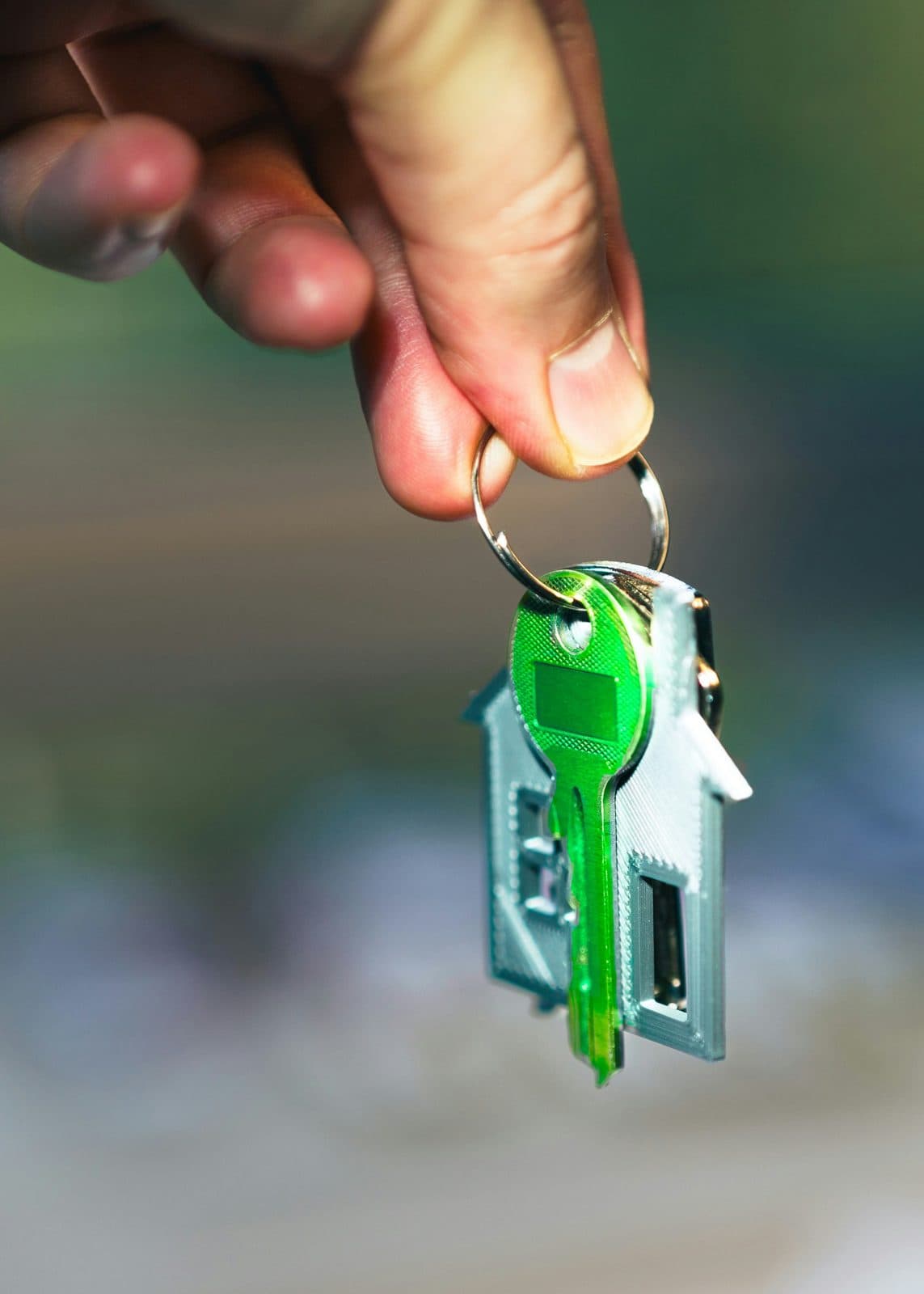 Mano con un portachiavi a forma di casa verde