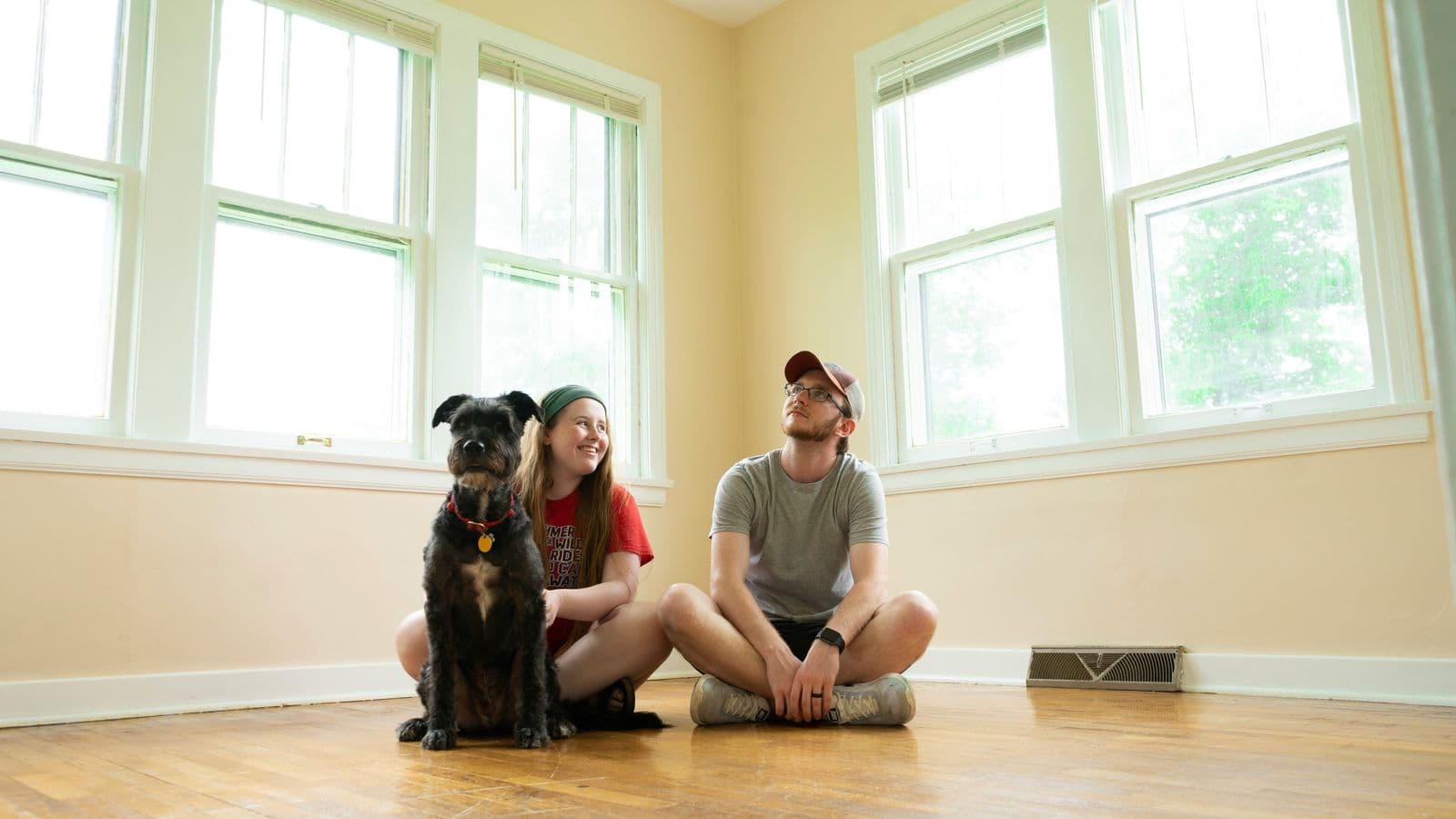 Due persone sedute sul pavimento di una stanza vuota con un cane