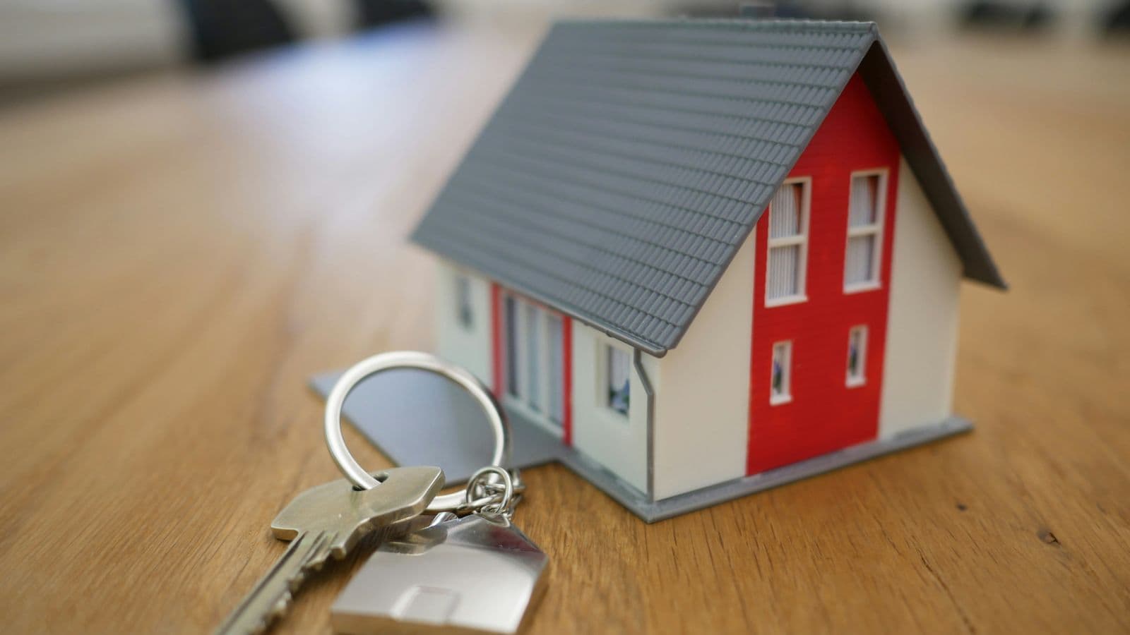 Modellino di casa con tetto grigio e pareti rosse accanto a un mazzo di chiavi